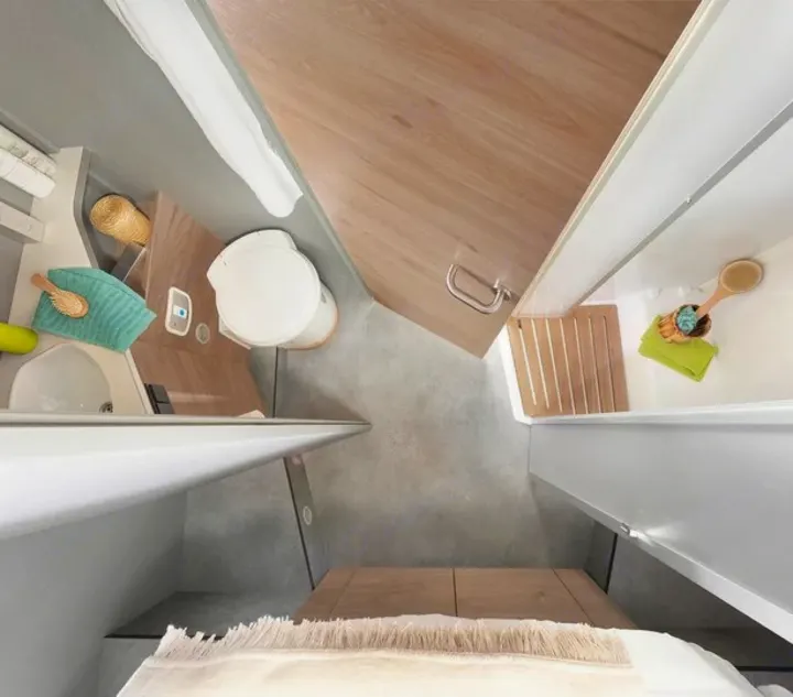This overhead view reveals a compact RV rental bathroom, featuring a white toilet, sink, and bathtub/shower area. Modern design optimizes space.. Dethleffs Juyst T 7052 2023