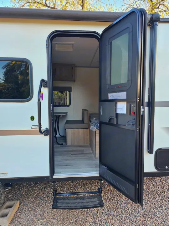RV rental: An open door invites you into this travel trailer, revealing its interior dinette, bed, and entry steps.. Keystone Coleman 17BX 2025