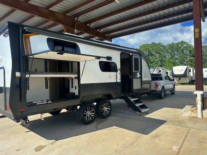 This spacious Ember Overlander RV rental travel trailer, with its side open to reveal bunk beds & storage, is hitched to a pickup.. Ember Overland 2023