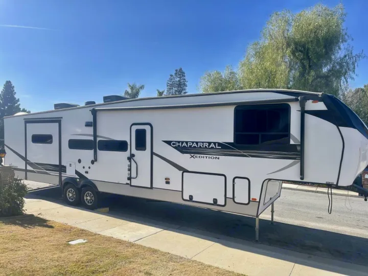 A large white Chaparral Xedition fifth-wheel RV rental is parked on a sunny street, featuring multiple windows and two doors.. Forest River Coachmen Chaparral Lite 2022