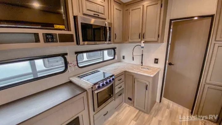 Modern RV rental kitchen featuring a microwave, stove, sink, ample light wood cabinets, and large windows.. Forest River Coachmen Chaparral Lite 2022