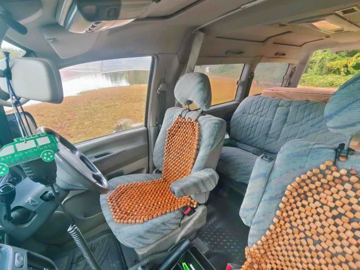 Inside a vintage RV rental adventure van, showing beaded seats, steering wheel, and an outdoor view.. MITSUBISHI Delica 1997