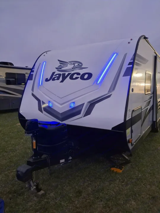 Bright blue lights illuminate the front of this Jayco RV rental at dusk, parked on green grass.. Jayco Jay Feather 2022