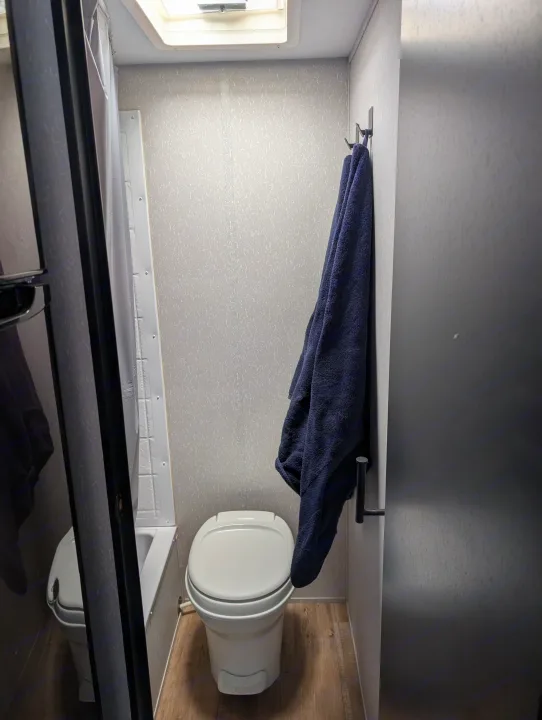 RV rental bathroom: A compact space with a toilet, partial shower, and a dark blue towel on hooks. Skylight visible above.. Forest River Cherokee Wolf Pup 2022