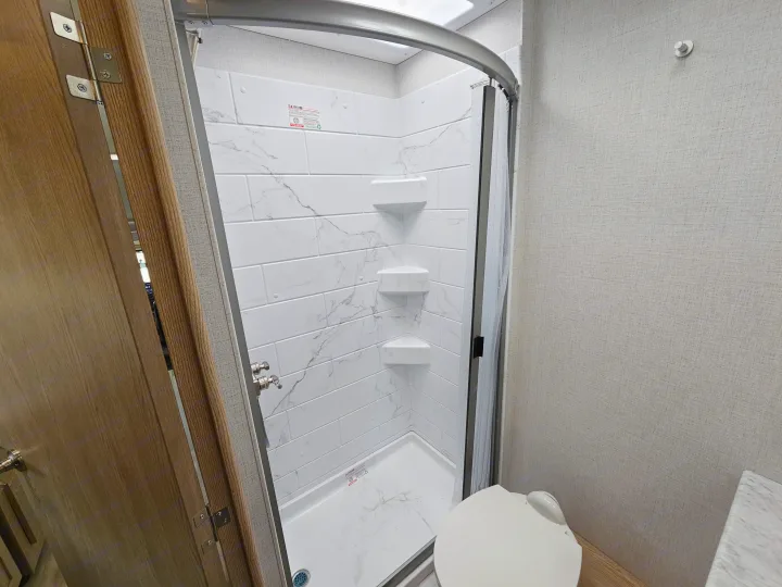 RV rental: Clean, compact bathroom with white marbled shower tiles, corner shelves, and a white toilet.. Thor Motor Coach Four Winds 2026