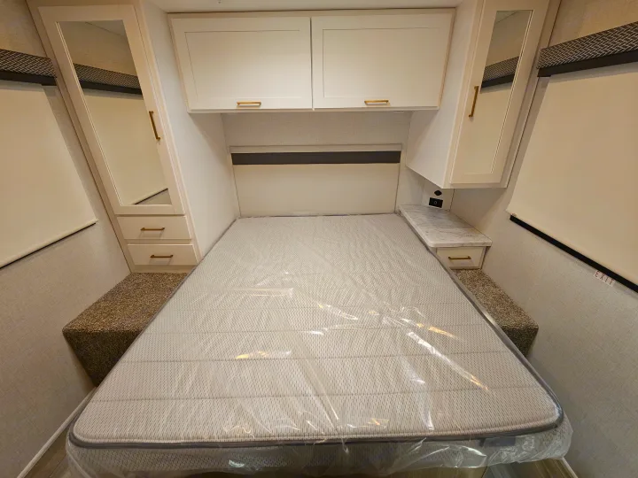 This RV rental bedroom features a new mattress, overhead cabinets, mirrored storage, and bedside drawers, offering compact and comfortable living.. Thor Motor Coach Four Winds 2026