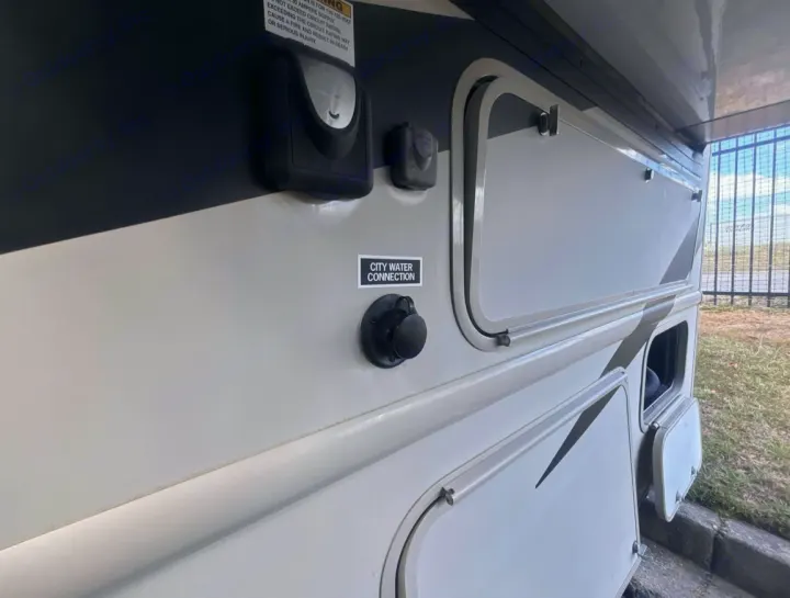 RV rental side showing the city water connection and utility hookups. Storage compartments are visible on this camper's exterior.. Thor Chateau Sprinter 2018
