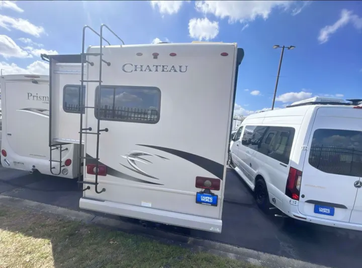 Rear view of a white Chateau RV rental, with a Sprinter van alongside, parked at an outdoor dealership lot under blue skies.. Thor Chateau Sprinter 2018