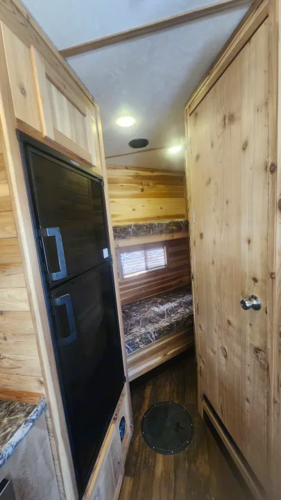 RV rental interior featuring wood paneling, refrigerator, bunk beds, and a floor fishing hole. A perfect blend of comfort and utility.. Ice Castle Fish Houses Toy Hauler 2022