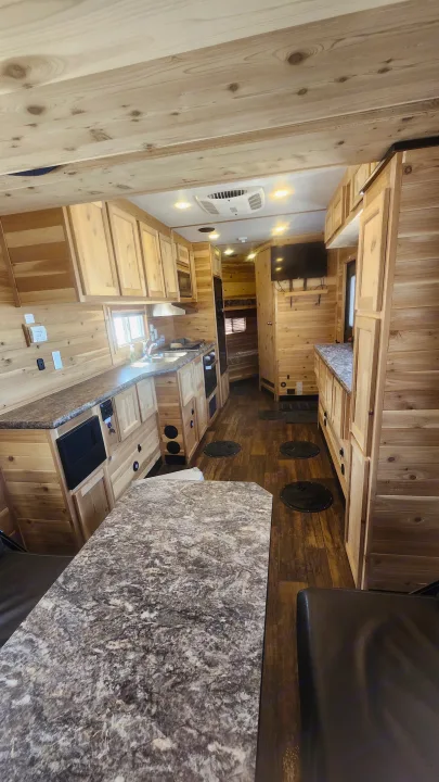 Spacious wood-paneled RV rental interior with kitchen, dining area, and multiple ice fishing holes.. Ice Castle Fish Houses Toy Hauler 2022
