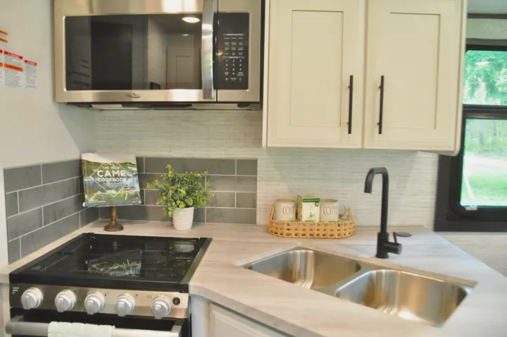This compact RV rental kitchen features modern amenities like a stainless steel microwave, stove, sink, and stylish backsplash.. Jayco Greyhawk 31F Bunkhouse 2025