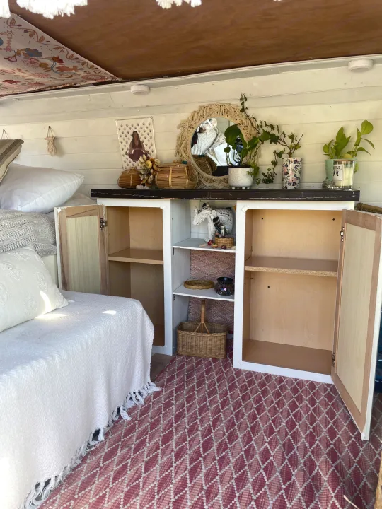 Bohemian RV rental interior featuring a daybed, open cabinets with decor, and a red geometric rug. Experience cozy travel.. Ford Econoline 150 2011