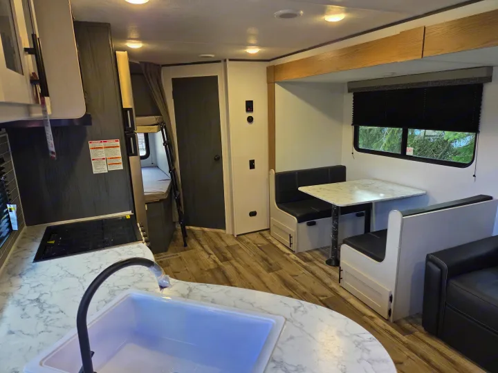 Step inside this modern RV rental showing a kitchen, dinette, and bunk beds, perfect for family travel.. Dutchmen Aspen Trail 2025