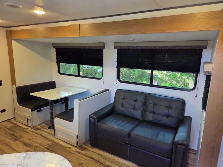 Experience comfort in this RV rental's modern interior, featuring a dinette booth, cozy sofa, and large windows.. Dutchmen Aspen Trail 2025