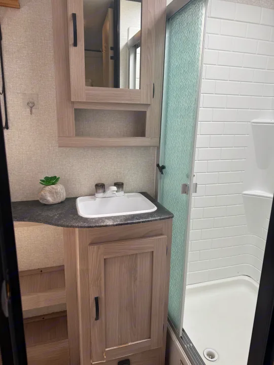 RV rental bathroom features: vanity, sink, mirrored cabinet, textured glass shower door, and white subway tile walls.. Forest River Coachmen Northern Spirit Ultra Lite 2023