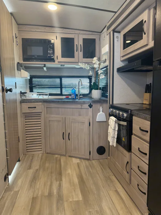 Modern RV rental kitchen featuring light wood cabinetry, microwave, sink, and stovetop for your mobile adventures.. Forest River Coachmen Northern Spirit Ultra Lite 2023