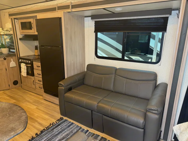 RV rental interior showcasing a kitchen with fridge & oven, and a dark grey reclining sofa.. Forest River Coachmen Northern Spirit Ultra Lite 2023