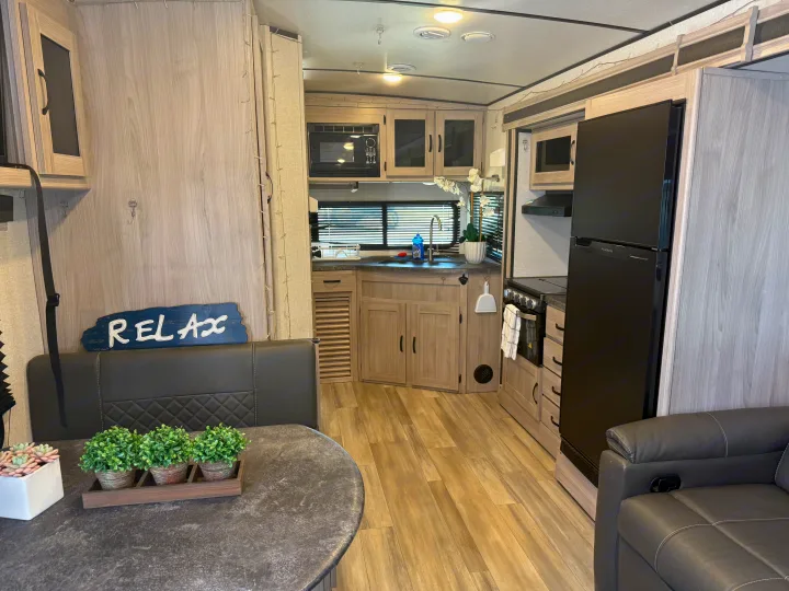Inside an RV rental: a bright kitchen and dining area with modern black appliances and light wood finishes.. Forest River Coachmen Northern Spirit Ultra Lite 2023
