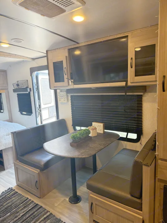 Cozy RV rental interior featuring a dinette, mounted TV, and adjacent bed area. Perfect for travel adventures.. Forest River Coachmen Northern Spirit Ultra Lite 2023