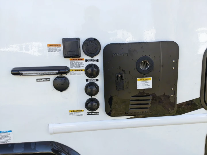 This RV rental's side panel shows utility connections including electrical, water, cable/satellite, and a water heater exhaust with safety warnings.. East to West Alita 2025
