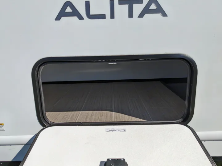 An Alita RV rental features a spacious, open exterior storage compartment with a wood-look floor, ready for gear.. East to West Alita 2025