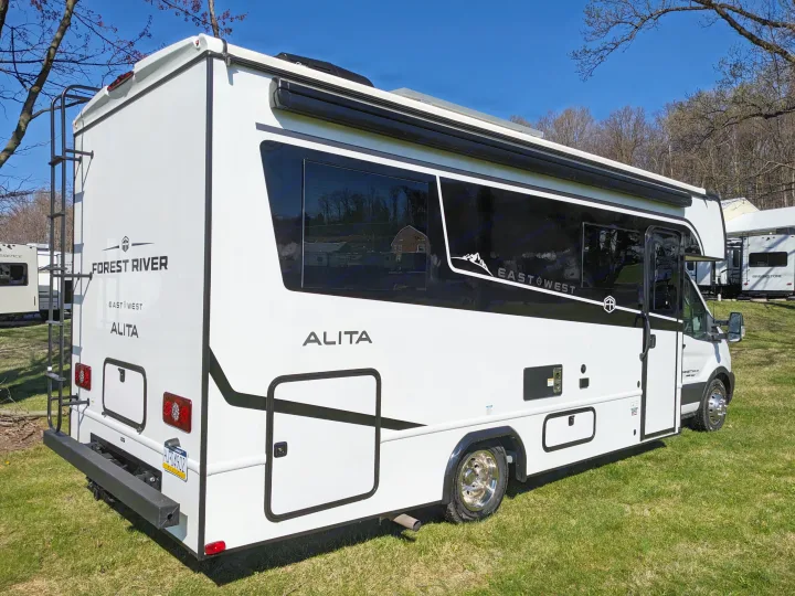 White Forest River East West Alita Class C RV rental, featuring a rear ladder & black side windows, parked on green grass.. East to West Alita 2025