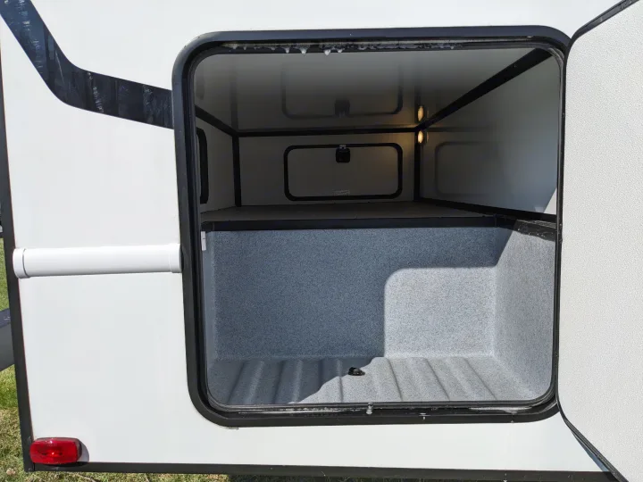Open RV rental storage compartment with grey lining, internal lights, and white exterior. Great for travel and camping gear.. East to West Alita 2025
