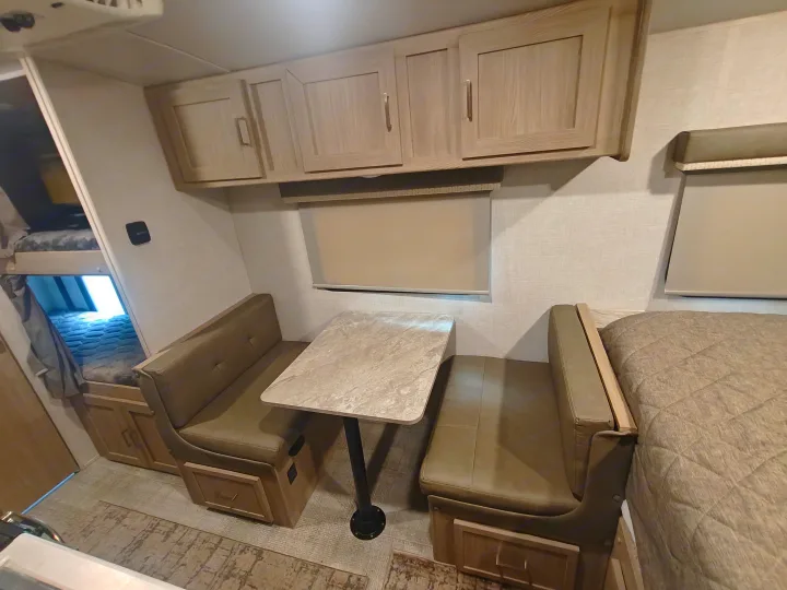 This RV rental interior features a dinette, bunk beds, overhead cabinets, and a main bed, showcasing compact living.. Geopro 19Bh 2021