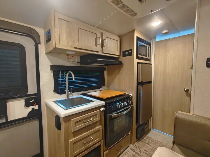 An RV rental interior showcasing a modern kitchen with sink, oven, microwave, and fridge, leading to a living area.. Geopro 19Bh 2021