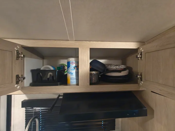 RV rental kitchen cabinets open, showing compact storage of dishes, cookware, and cleaning supplies. Ideal for travel.. Geopro 19Bh 2021