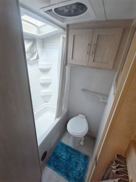 Compact rv rental bathroom with shower, toilet, overhead cabinets, and a blue bathmat.. Geopro 19Bh 2021