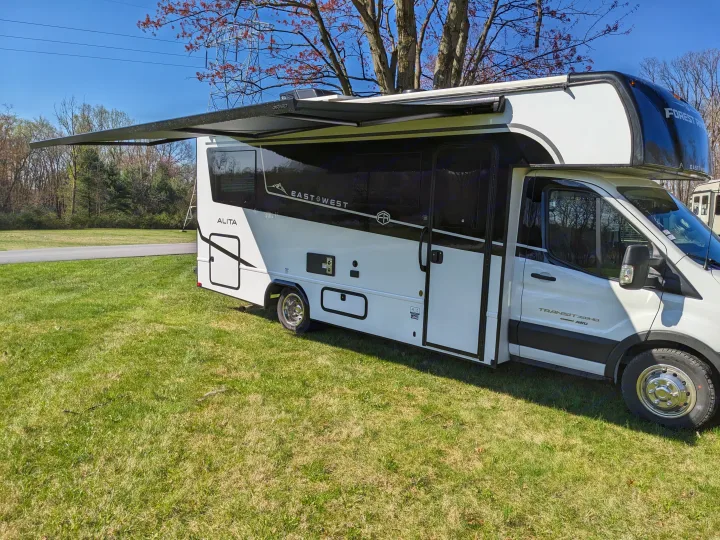 White & black East & West Alita RV rental with an extended awning, parked on green grass. Ideal for travel & outdoor adventures.. East to West Alita 2025