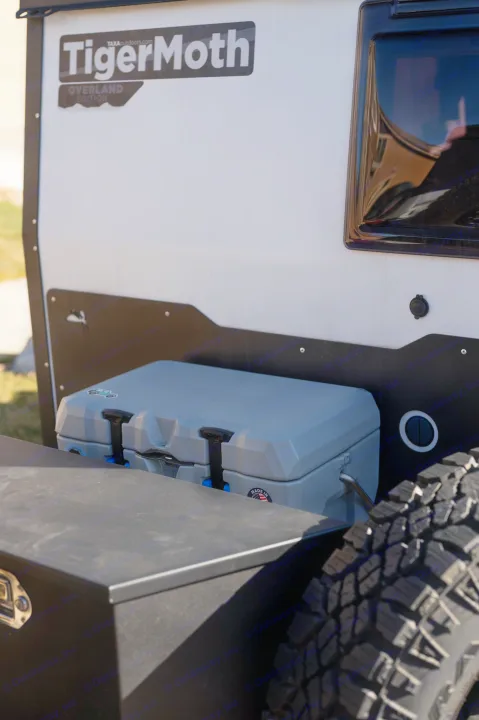 TigerMoth Overland Edition travel trailer, an RV rental, with a cooler, storage box, and rugged tire.. TAXA Tiger Moth 2023