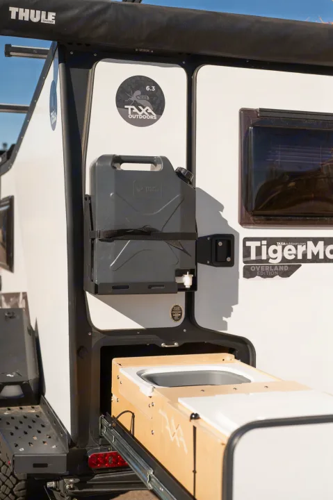 Side view of a white RV rental with a mounted water tank and a pull-out kitchen, ideal for outdoor trips.. TAXA Tiger Moth 2023