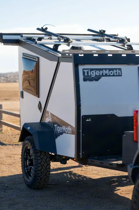 Close-up of a white and black TigerMoth overland trailer with off-road tires and roof racks. Ideal for an RV rental outdoor adventure.. TAXA Tiger Moth 2023
