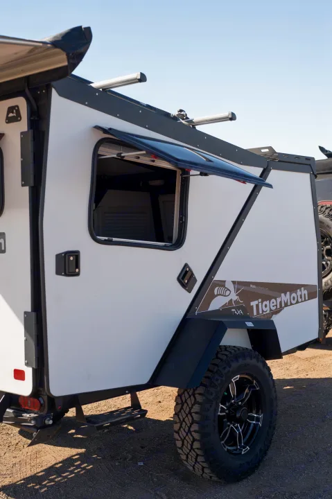 This white TigerMoth overland RV rental features an open window, rugged tire, and black accents, ready for adventure.. TAXA Tiger Moth 2023