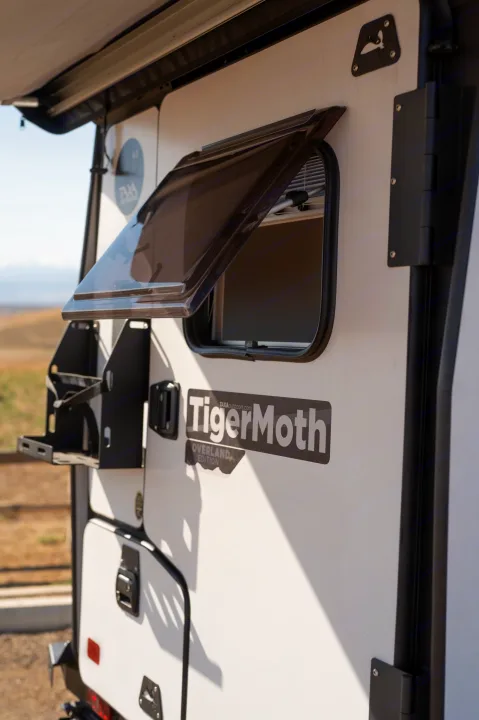 Close-up of a white TigerMoth Overland Edition off-road camper, ideal for an RV rental adventure, featuring an open window and side rack.. TAXA Tiger Moth 2023