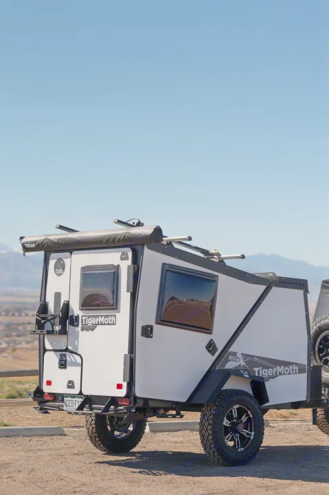A white and black TigerMoth overland trailer, ideal for an RV rental, parked on dirt with mountains in the background. Ready for off-road camping.. TAXA Tiger Moth 2023