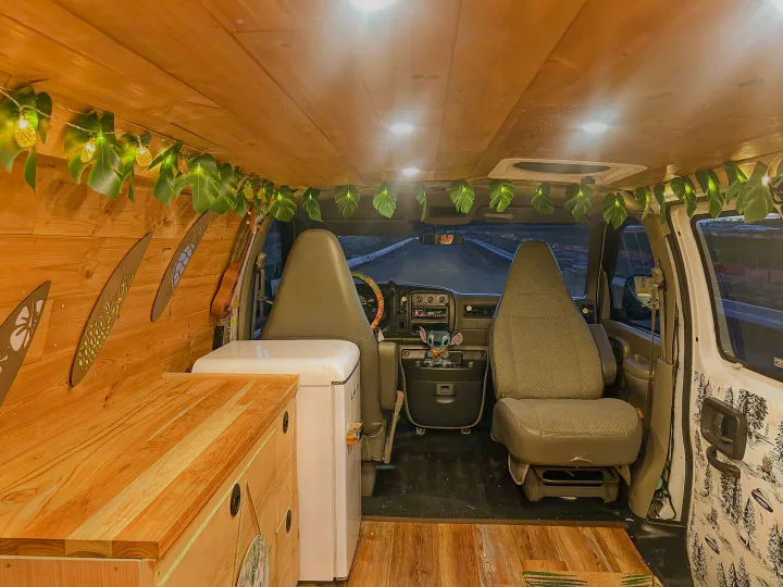 Explore this unique RV rental interior: wooden walls, leafy string lights, mini-fridge, and front cab.. Chevrolet Express 1999