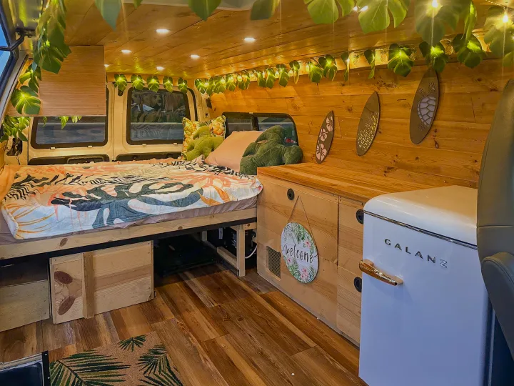 Tropical-themed RV rental interior with leaf lights, patterned bedding, wooden walls, and a retro fridge.. Chevrolet Express 1999