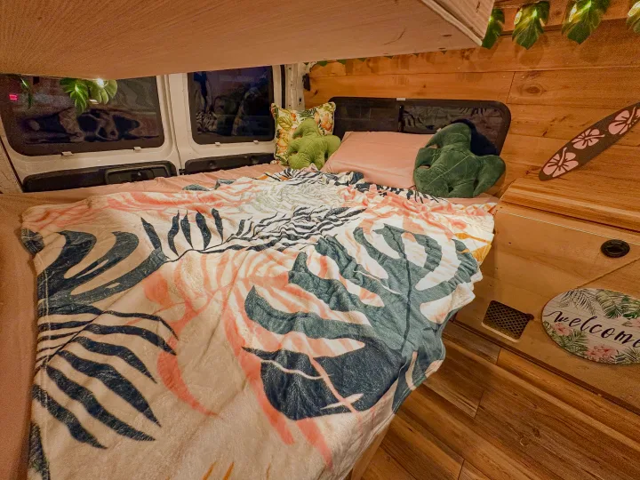 Inside a stylish RV rental, a comfy bed with tropical patterns, leaf pillows, and wood details create a cozy retreat.. Chevrolet Express 1999