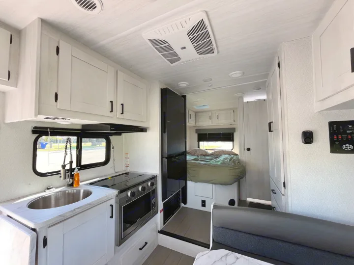 Modern RV rental interior: bright kitchen with sink, stove, microwave, leading to a cozy bedroom & living area.. East to West Entrada 210NS 2025