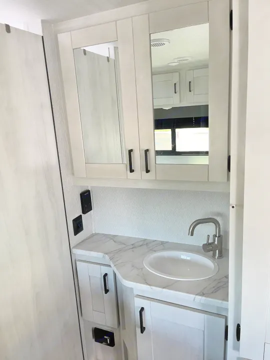 Inside an RV rental: a bright bathroom vanity with a marble-look counter, sink, and medicine cabinet.. East to West Entrada 210NS 2025