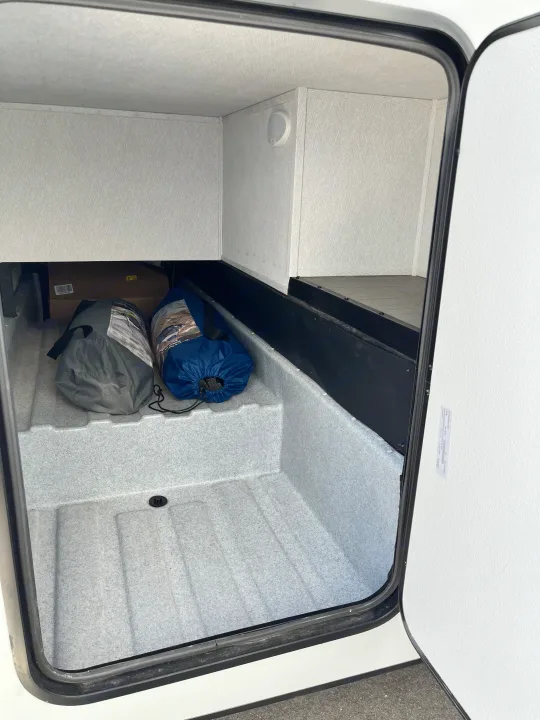 Spacious RV rental storage compartment, ready for adventure. Organized interior with light, showing packed gear bags and box.. East to West Entrada 210NS 2025