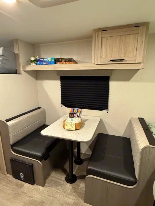 An inviting RV rental dinette with a s'mores welcome basket, board games on a shelf, and comfy black & grey seating.. Heartland Trail Runner 2025