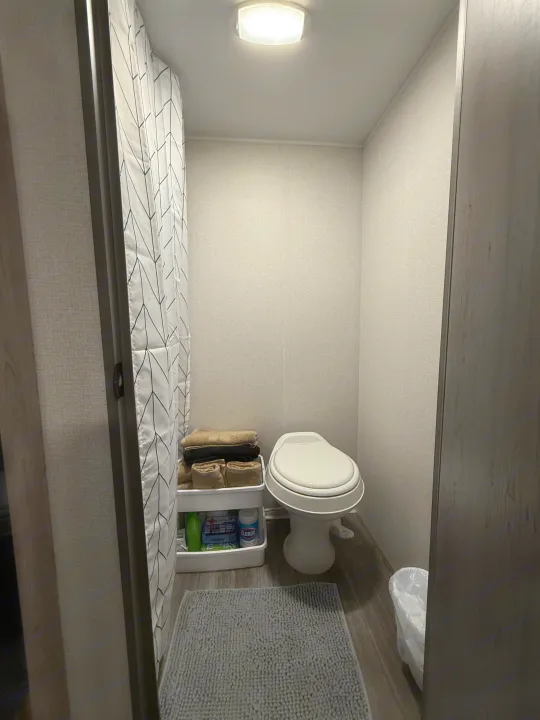 Compact RV rental bathroom featuring a toilet, geometric shower, and organized storage for toiletries.. Heartland Trail Runner 2025
