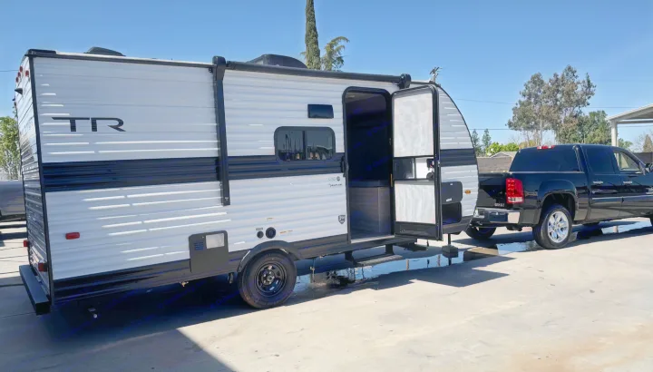 RV rental: A clean, white Heartland travel trailer with an open door, hitched to a black GMC pickup truck on concrete.. Heartland Trail Runner 2025