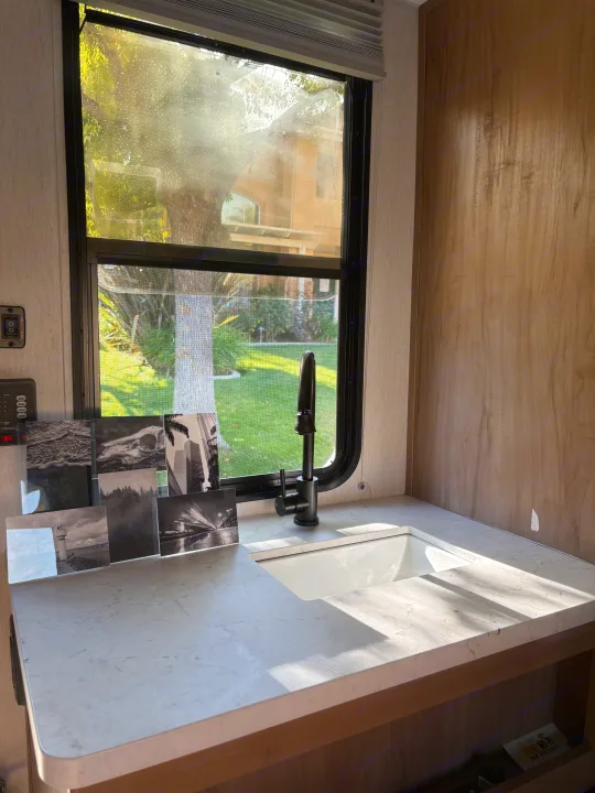 Bright RV rental kitchen with a window view of a yard, featuring a modern sink, counter, and black & white art.. Forest River Cherokee Wolf Den 16EV 2024