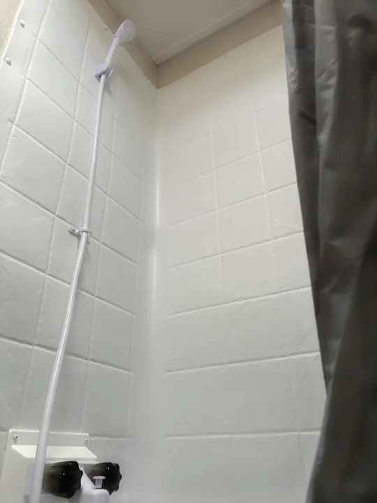 Inside a compact RV rental shower: white molded walls, a hand-held shower, and dark water controls are visible.. Forest River Cherokee Wolf Den 16EV 2024