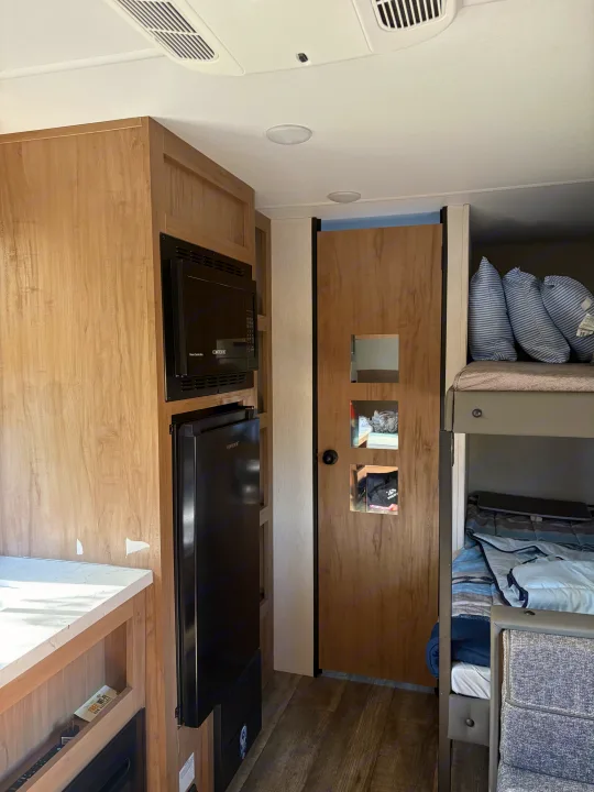 Experience comfort in this RV rental interior: featuring a light wood kitchen with microwave, fridge, and bunk bed area.. Forest River Cherokee Wolf Den 16EV 2024